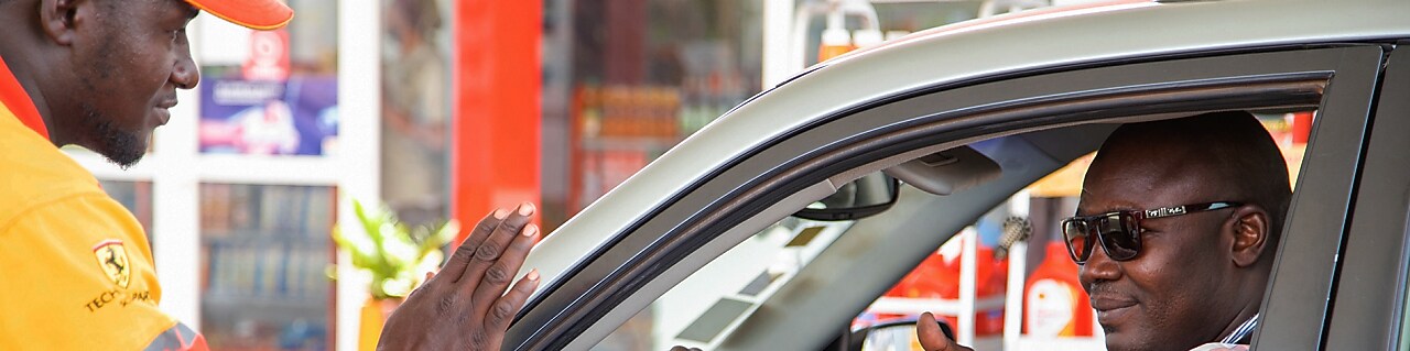 Employé Shell accueillant un automobiliste souriant sur la piste de distribution