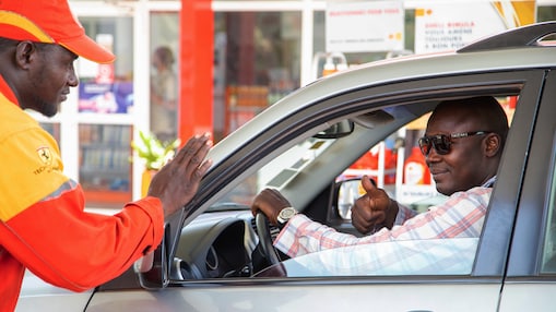 Employé Shell accueillant un automobiliste souriant sur la piste de distribution